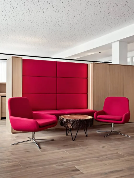 Moderner Büroraum mit rotem Softline Sitzbereich, zwei drehbaren Sesseln und einem Baumstamm-Couchtisch, Referenz