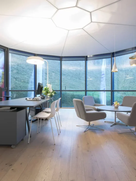 Modernes Büro mit großem Tisch, ergonomischem Stuhl, vier grauen Lounge-Sesseln um runden Tisch und, Referenz