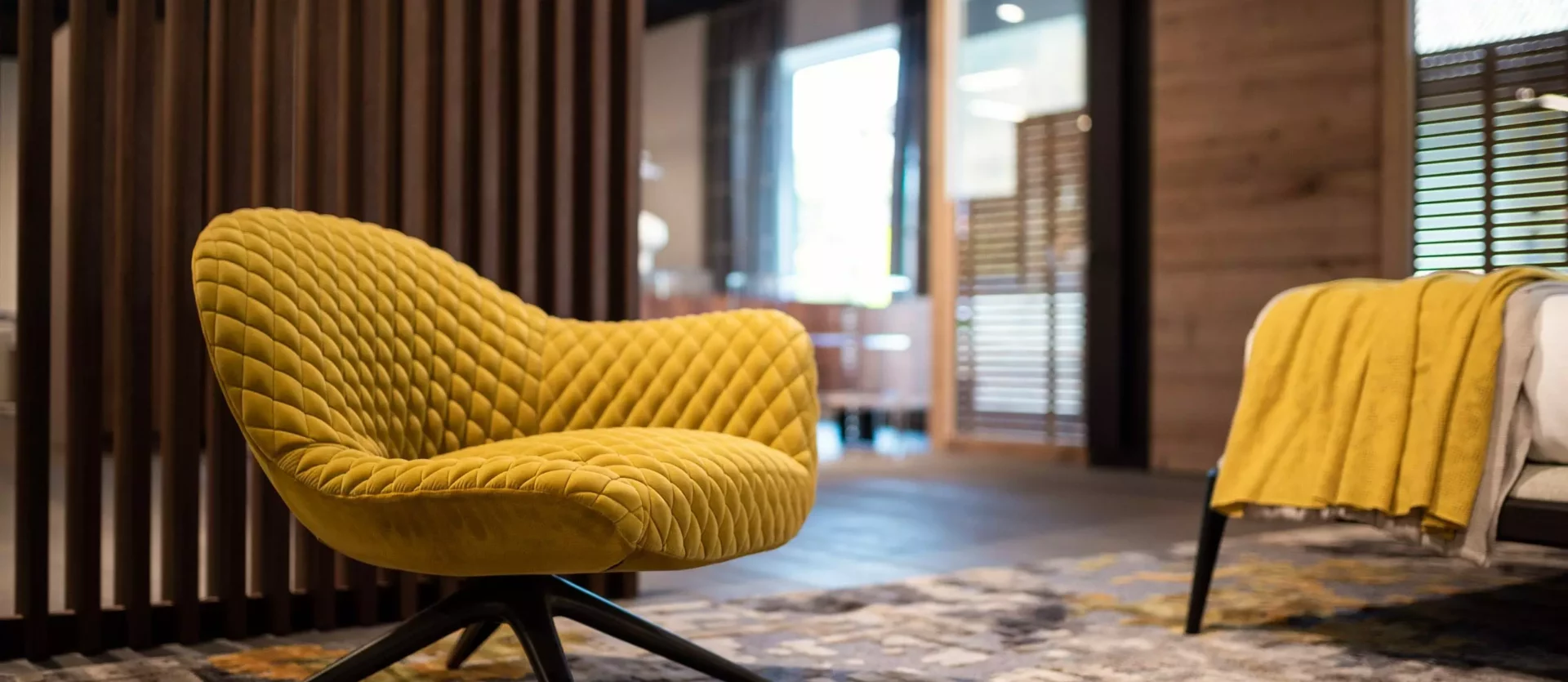 Gelber Leslie Aston Sessel von Minotti auf gemustertem Teppich im modernen Möbelstudio mit Holzpaneelen und Wohnraumplanung