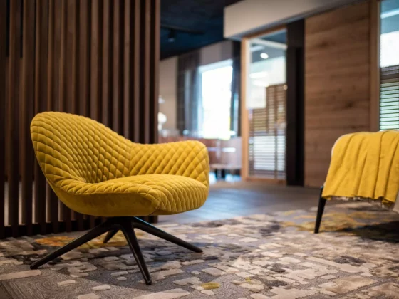 Gelber Leslie Aston Sessel von Minotti auf gemustertem Teppich im modernen Möbelstudio mit Holzpaneelen und Wohnraumplanung