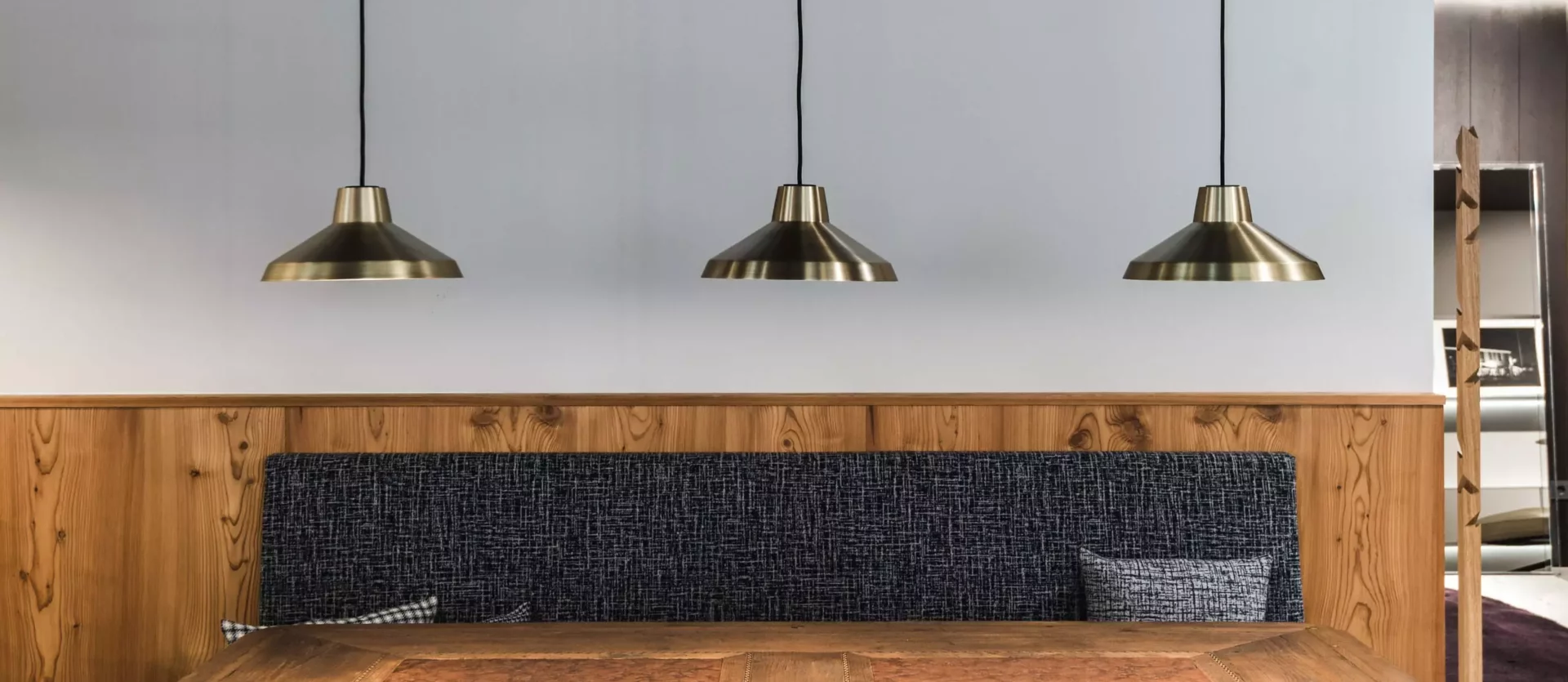 Essbereich mit rustikalem Holztisch, gepolsterter Sitzbank, drei goldfarbenen Hängelampen und Holzvertäfelung, Poliform