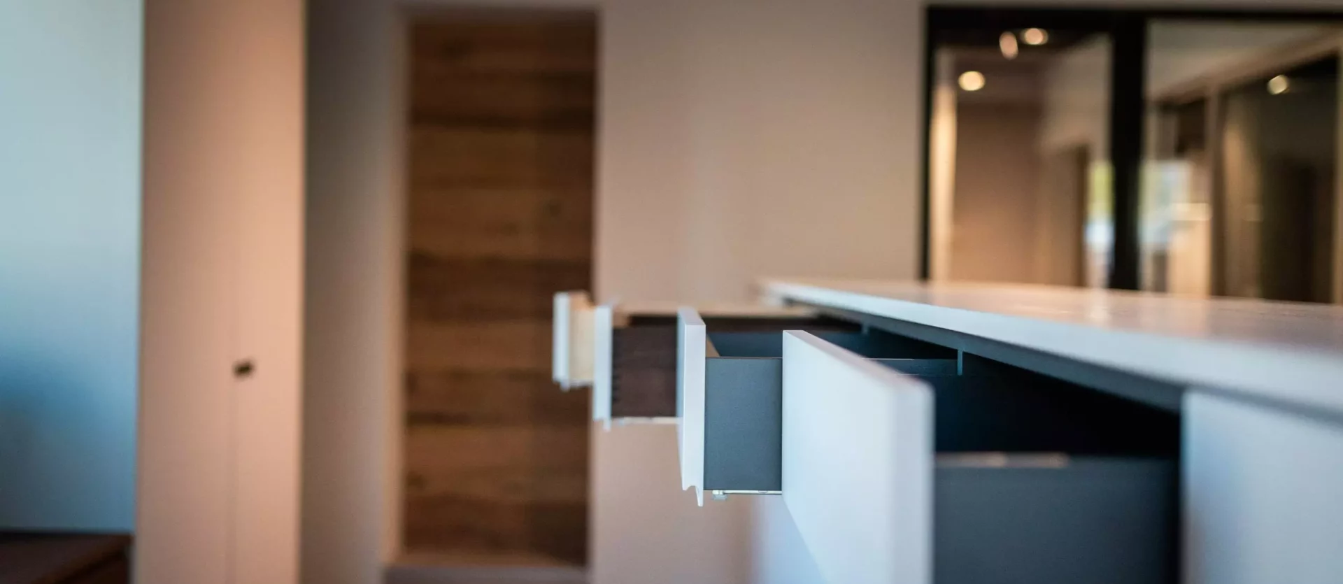 Offene Schubladen einer modernen weißen Kücheninsel in einem Innenraum mit Holzfußboden und minimalistischer, Poliform