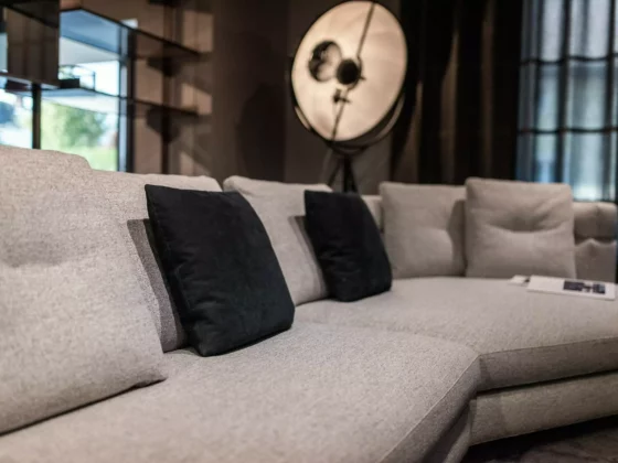 Großes graues Polstermöbel mit schwarzen Kissen vor Fenster und Stehlampe im modernen Möbelstudio mit, Poliform