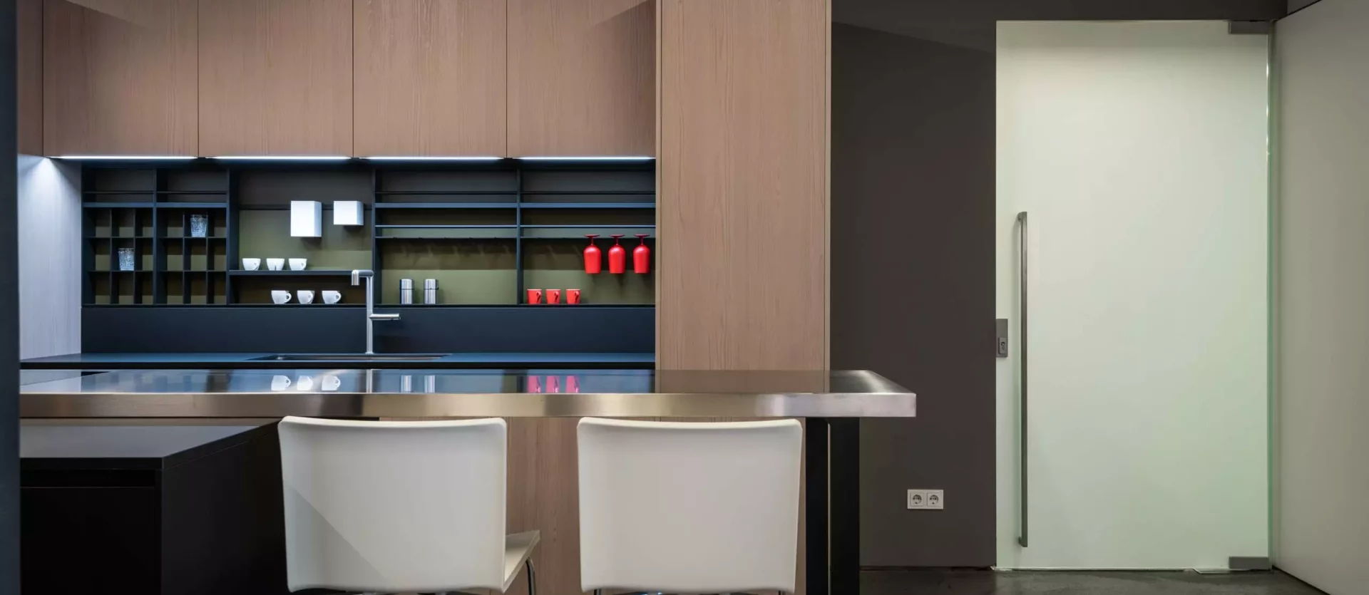 Moderne Poliform Küche Alea mit Lärchenholzfronten, Edelstahlarbeitsplatte, Küchenbar und weißen Barhockern im Showroom