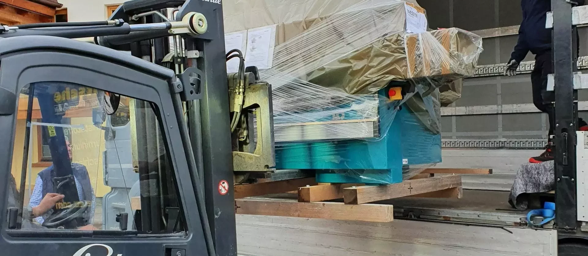 Gabelstapler der Marke Linde lädt verpackte Tischlereimaschine in Lkw, Außenbereich vor Holzhaus in Altenmarkt Pongau
