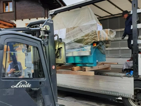 Gabelstapler der Marke Linde lädt verpackte Tischlereimaschine in Lkw, Außenbereich vor Holzhaus in Altenmarkt Pongau
