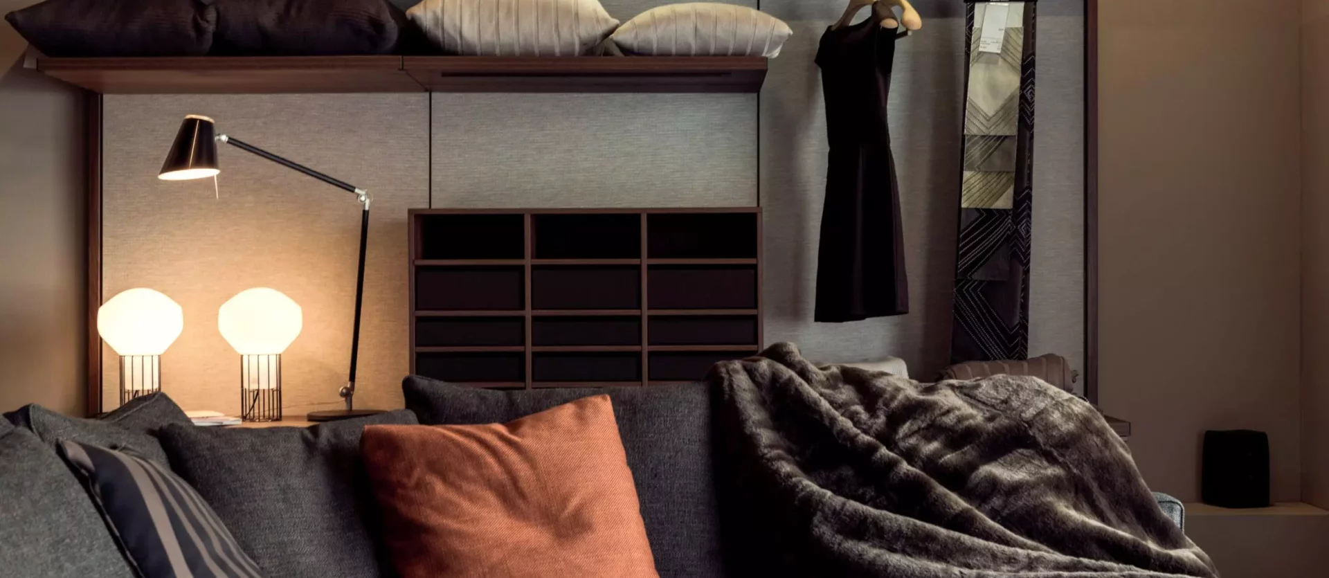 Moderner Wohnraum mit grauem Sofa, farbigen Kissen, Fell-Decke, Wandregal, Designerlampen und schwarzem, Innenarchitekt