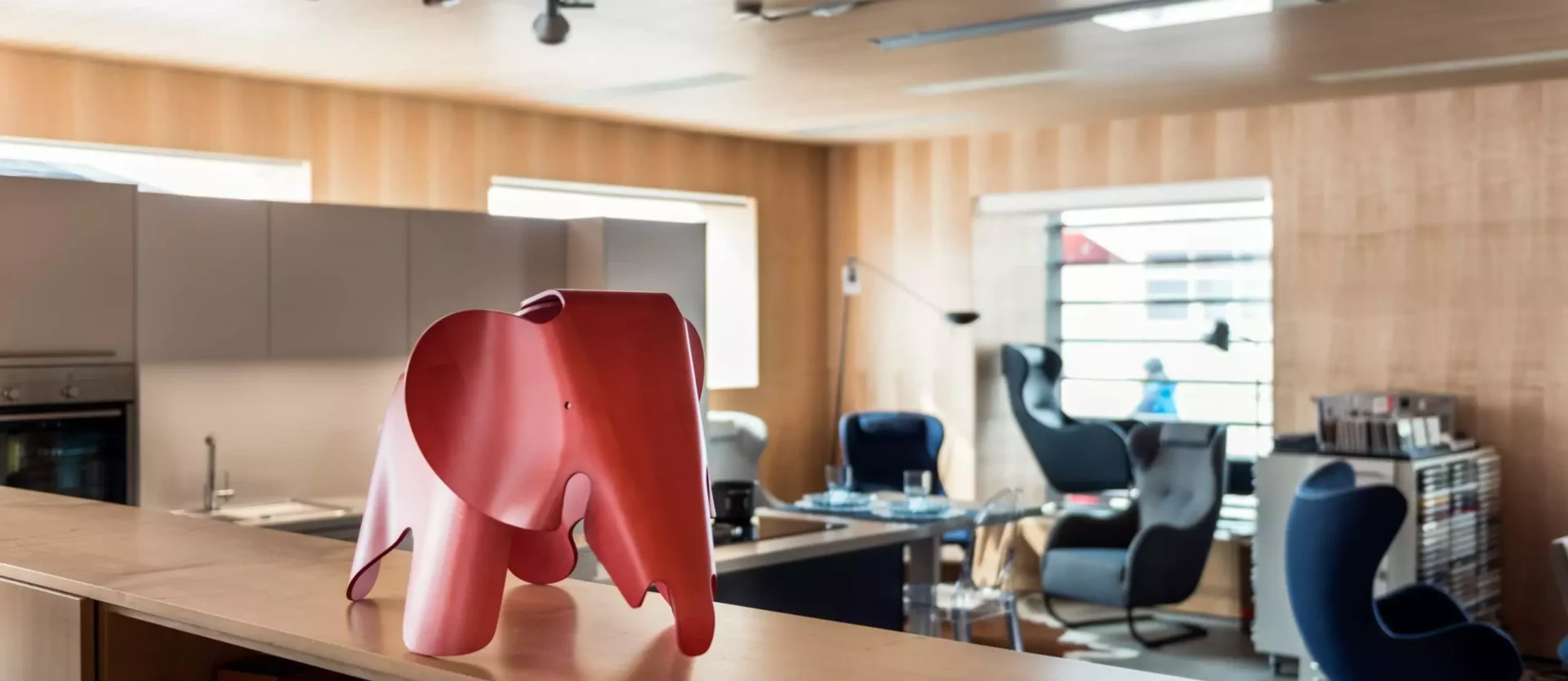 Moderner Showroom mit Designermöbeln, rotem Elephant-Objekt im Vordergrund, Sitzgruppen und Holzverkleidung, Innenarchitekt