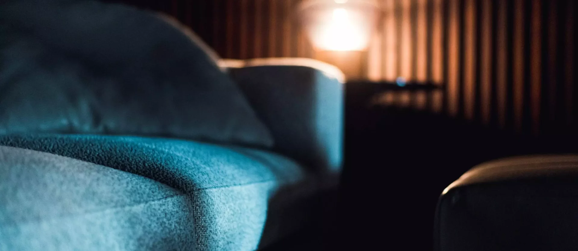 Nahaufnahme eines blauen Polstermöbels vor dunkler Holzlamellenwand mit warmem Licht im Hintergrund im, Innenarchitekt