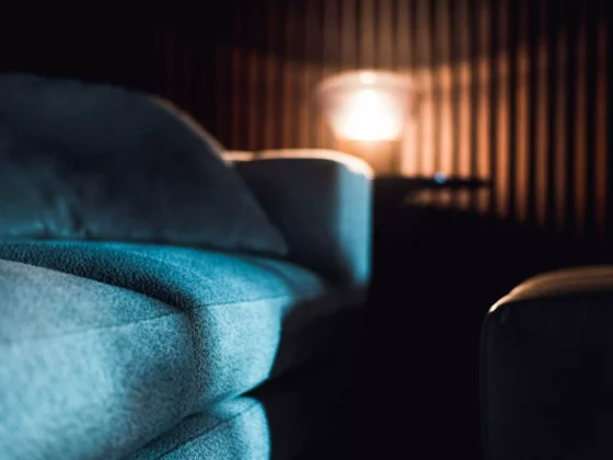 Nahaufnahme eines blauen Polstermöbels vor dunkler Holzlamellenwand mit warmem Licht im Hintergrund im, Innenarchitekt