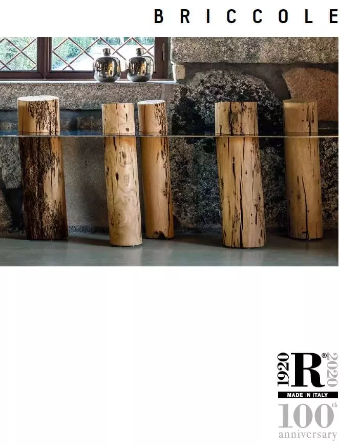 Riva1920 Briccole Kollektion Glastisch mit massiven Holzstämmen als Tischbeine vor rustikaler Steinwand im Möbelstudio für