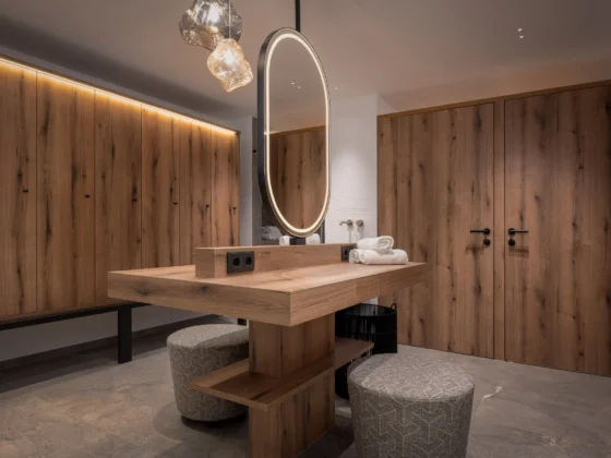 Moderner Umkleideraum mit maßgefertigten Holzschränken, zentralem Holz-Tisch mit beleuchtetem Spiegel und, Pongauerhof