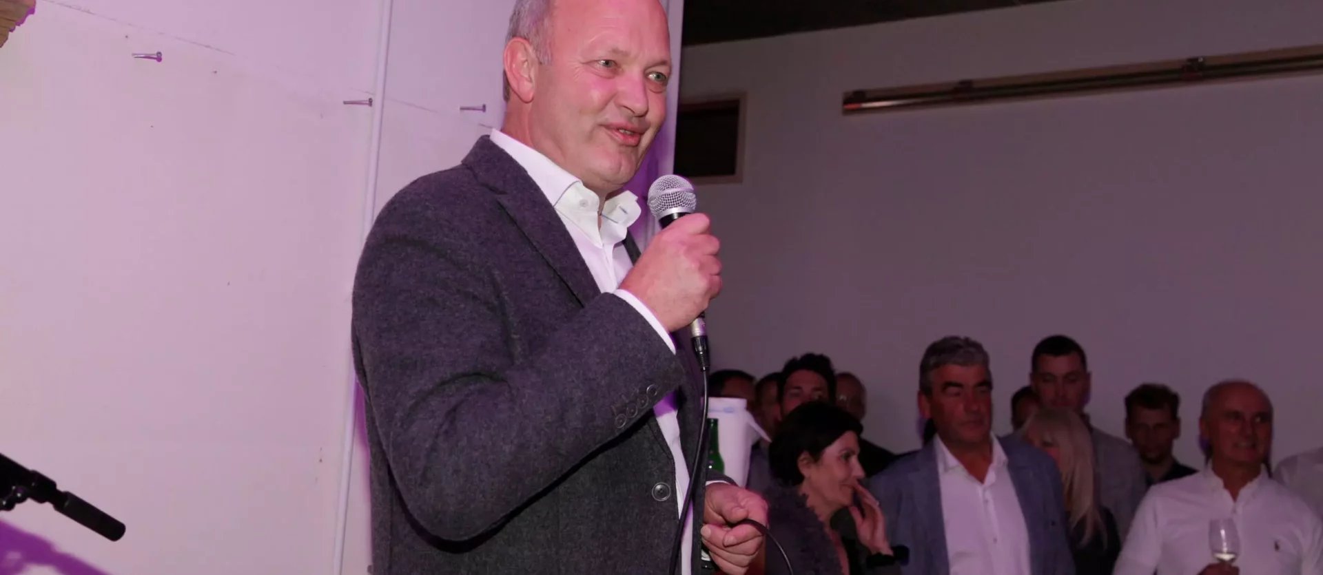 Mann im grauen Sakko hält Mikrofon und spricht vor Publikum bei Veranstaltung im Möbelstudio Showroom mit, Fest