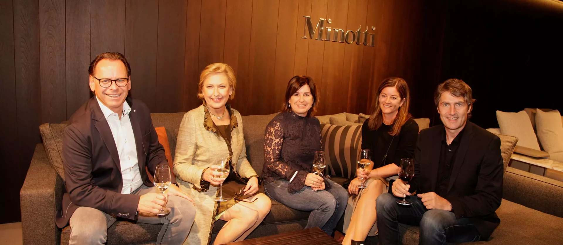 Fünf Personen sitzen auf einer grauen Couch im Minotti Showroom und halten Weingläser in der Hand, moderne, Fest