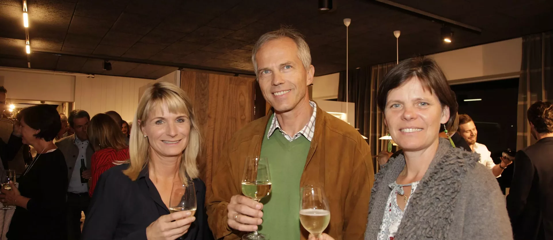 Drei Personen mit Weingläsern in einem modernen Showroom für Innenarchitektur und Designermöbel von Minotti und, Fest