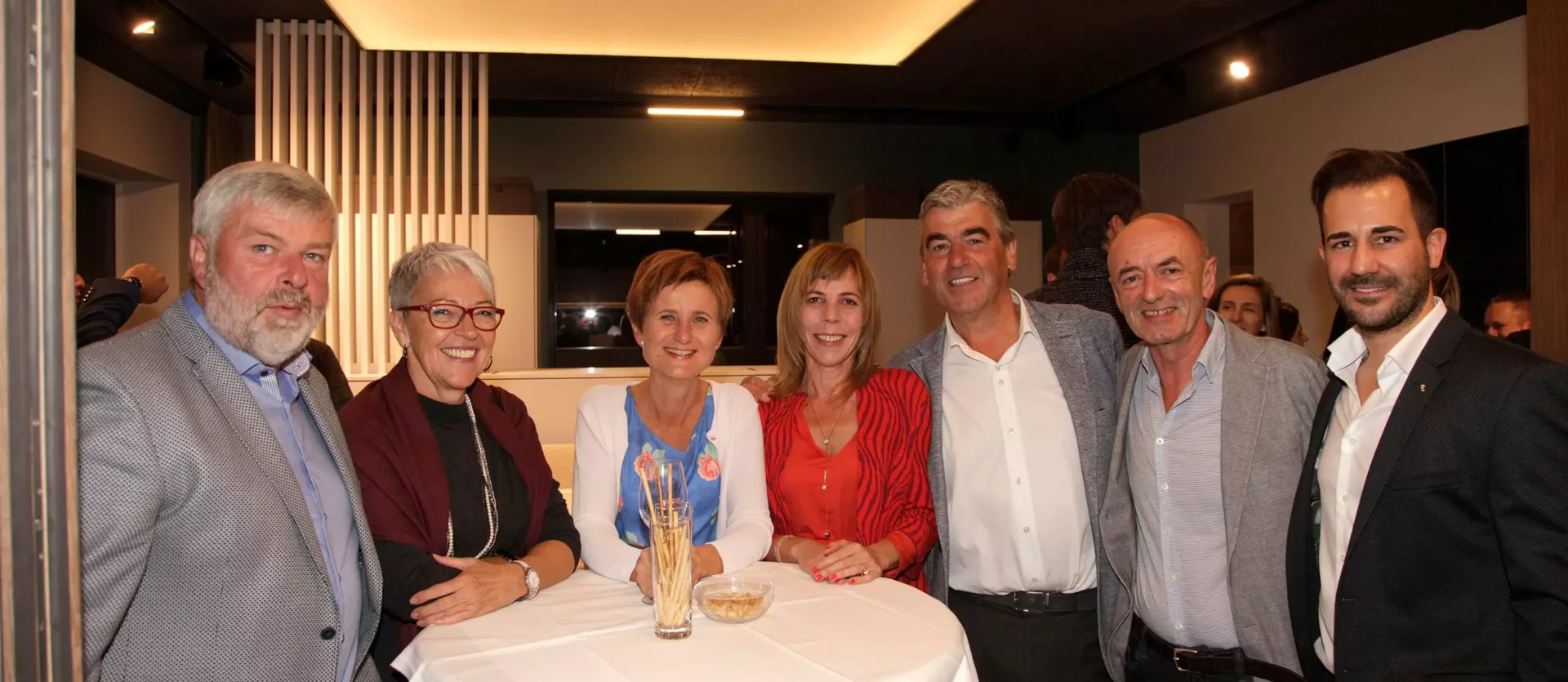 Gruppe von sieben Personen im Showroom des Möbelstudios Studio Reiter, stehend um einen Tisch mit Snacks, moderne, Fest