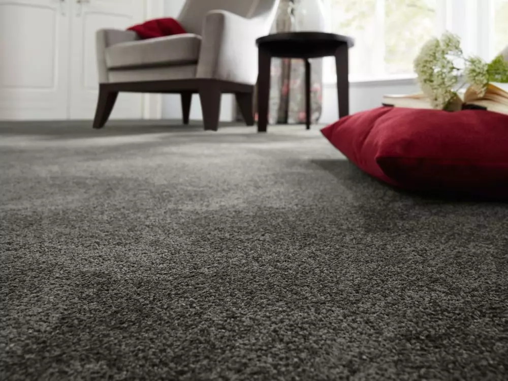 Weicher grauer Teppichboden im Wohnzimmer mit grauem Sessel, schwarzem Beistelltisch und rotem Kissen im Möbelstudio