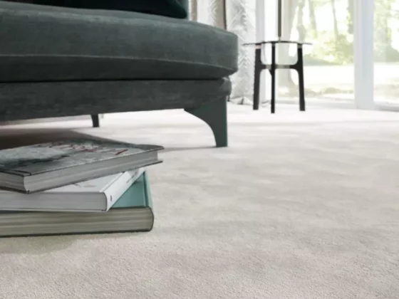 Nahaufnahme eines grünen Sofafusses neben einem Stapel Bücher auf hellem Teppichboden in modernem Wohnraum mit, Möbel