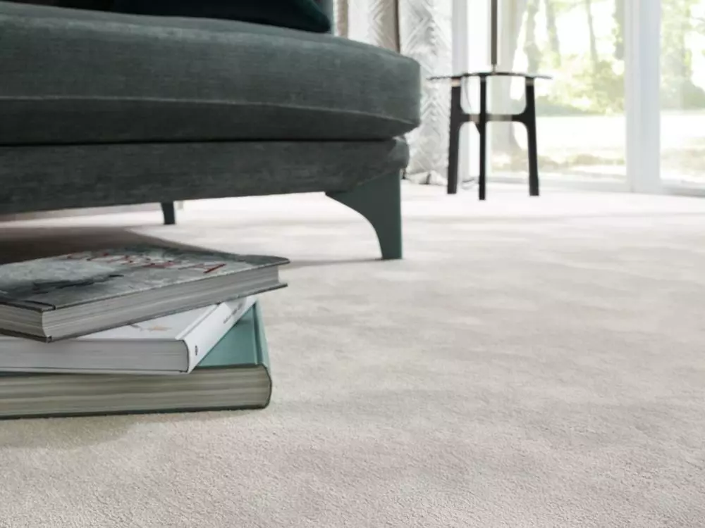 Nahaufnahme eines grünen Sofafusses neben einem Stapel Bücher auf hellem Teppichboden in modernem Wohnraum mit, Möbel