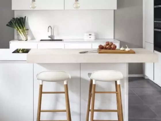 Moderne weiße Küche mit Holzarbeitsplatte, zwei Barhockern und minimalistischer Innenarchitektur im Möbelstudio-Showroom