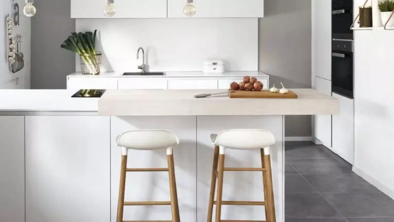 Moderne weiße Küche mit Holzarbeitsplatte, zwei Barhockern und minimalistischer Innenarchitektur im Möbelstudio-Showroom