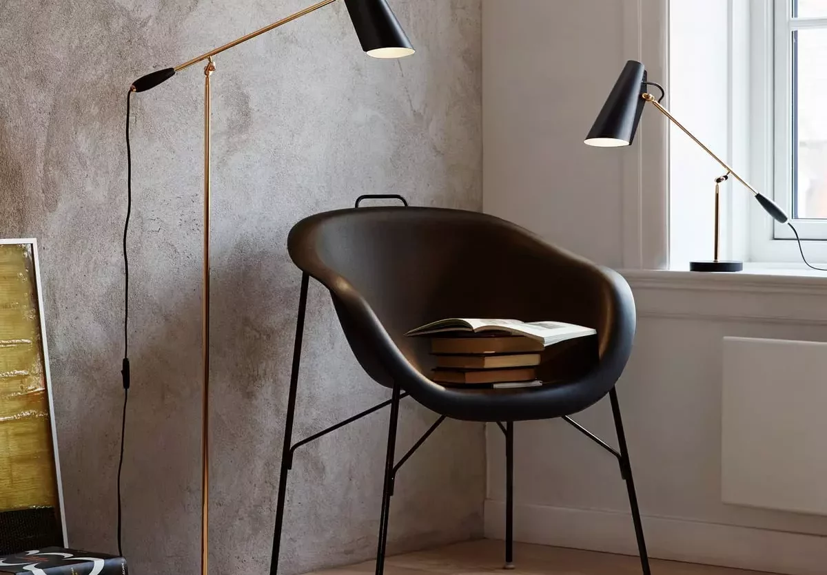 Schwarzer Design-Sessel mit Büchern darauf, daneben Stehlampe und Tischlampe mit schwarzem Schirm vor strukturierter, Möbel