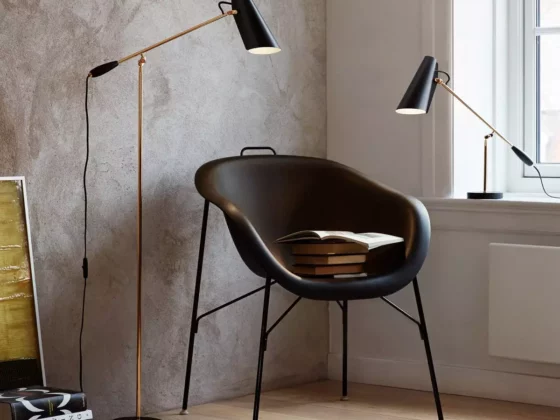 Schwarzer Design-Sessel mit Büchern darauf, daneben Stehlampe und Tischlampe mit schwarzem Schirm vor strukturierter, Möbel