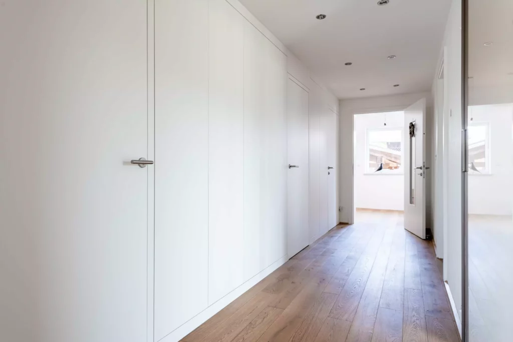 Moderner Flur mit maßgefertigten weißen Einbaukästen und Türen, hellem Holzboden und offener Tür zum, Rimadesio