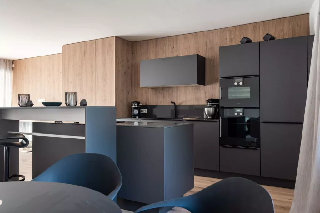 Moderne schwarze Küche mit Massivholz-Wandverkleidung, Kücheninsel, Einbaugeräten und Sitzbereich im Möbelstudio M-Studio