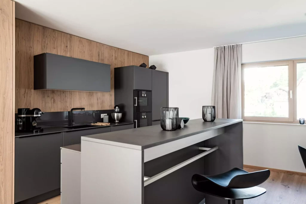 Moderne schwarze Küche mit Massivholz-Wandverkleidung, Kücheninsel und Barhocker in hellem Wohnraum mit Fenster, Möbelstudio