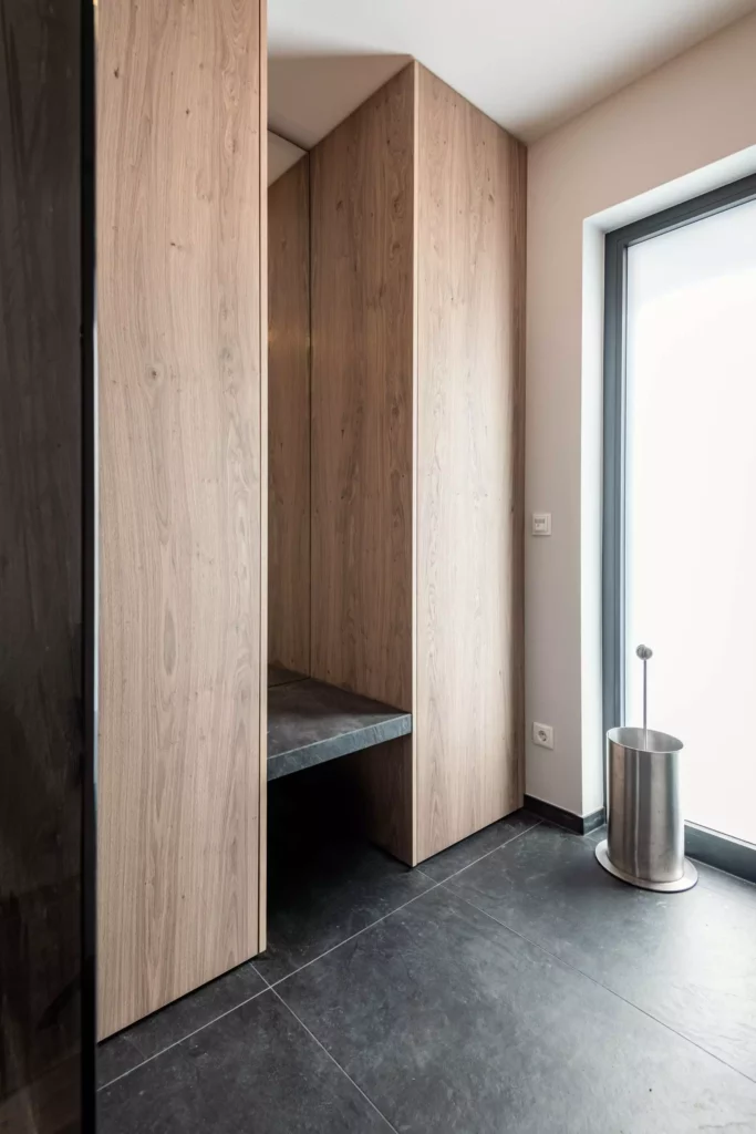 Eingangsbereich mit maßgefertigtem Holzschrank und Sitzbank aus dunklem Stein, schwarzer Bodenfliese und, Möbelstudio