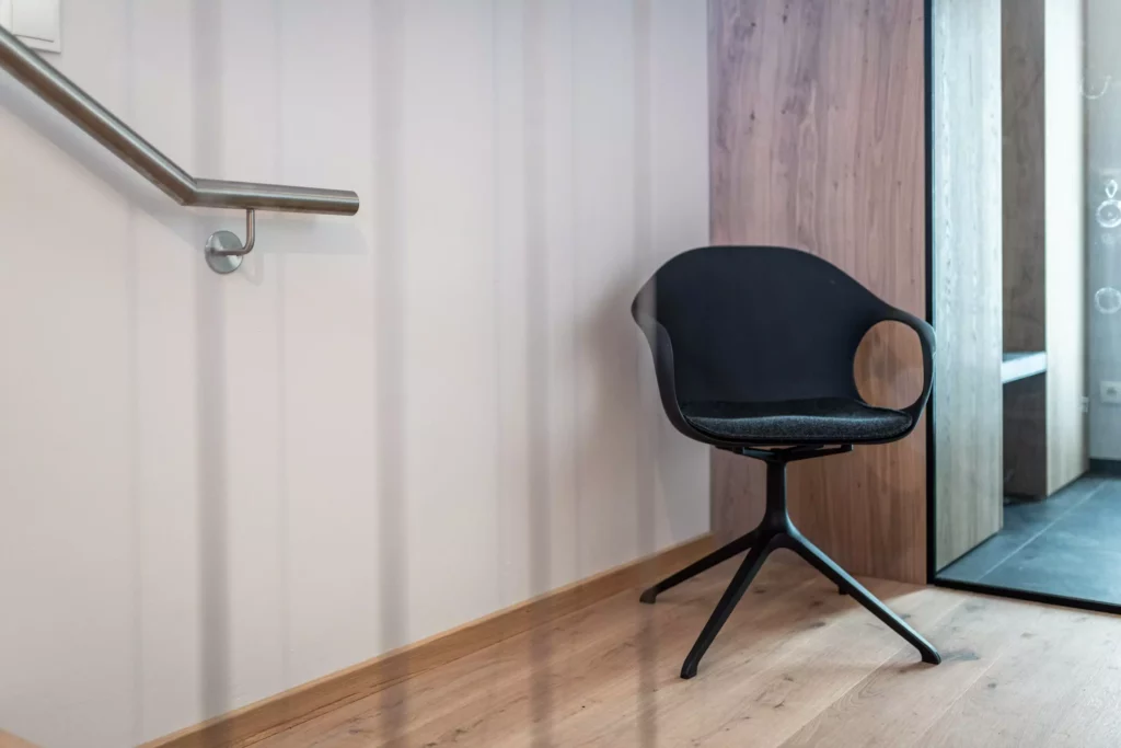 Schwarzer Designstuhl mit Armlehnen aus Kunststoff vor Holzpaneel und Spiegel in modernem Innenraum mit, Möbelstudio