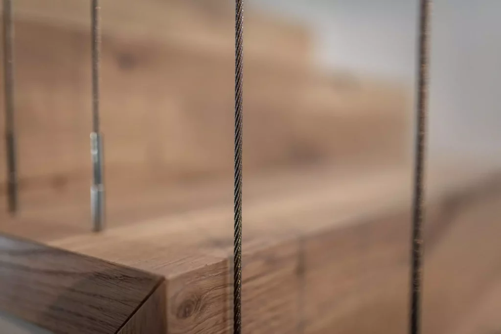 Nahaufnahme einer massiven Holzkante mit Stahlseilen, Detail einer maßgefertigten Innenarchitektur-Lösung im Möbelstudio