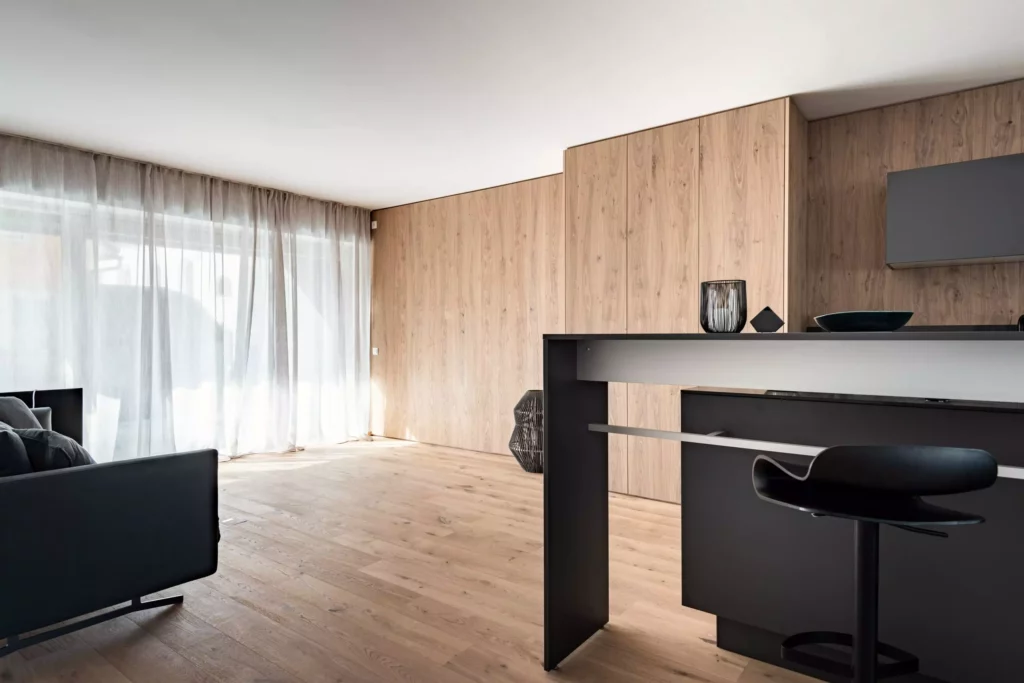 Moderner Wohnraum mit maßgefertigter schwarzer Kücheninsel, Barhocker und Holzverkleidung von M-Studio Reiter, Möbelstudio