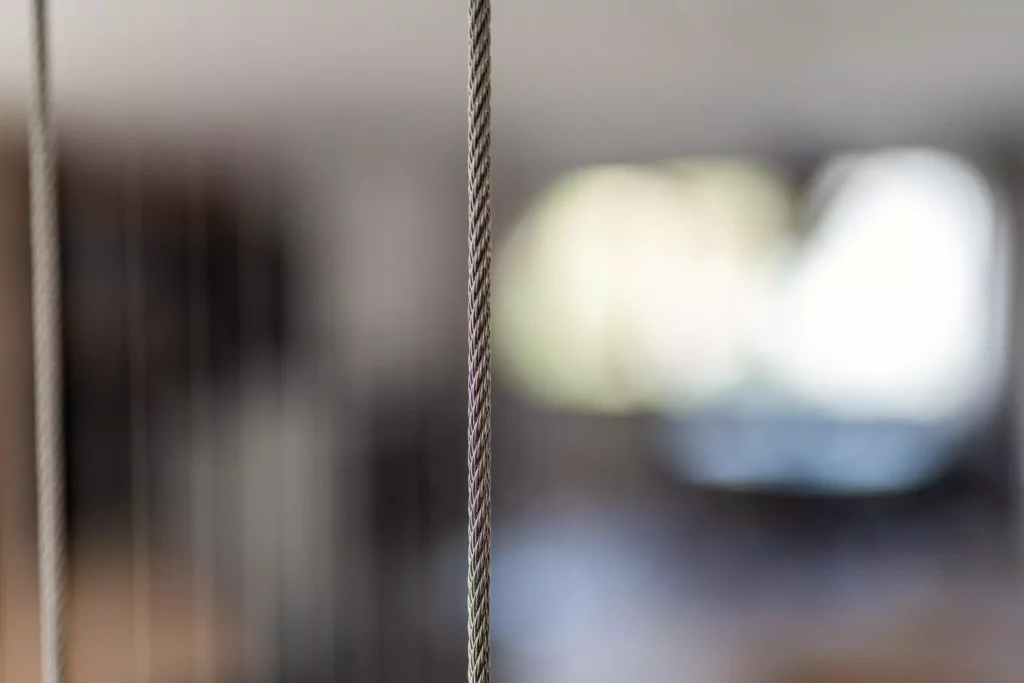 Nahaufnahme eines geflochtenen Stahlseils vor unscharfem Hintergrund in einem modernen Innenraum mit Möbelstudio und