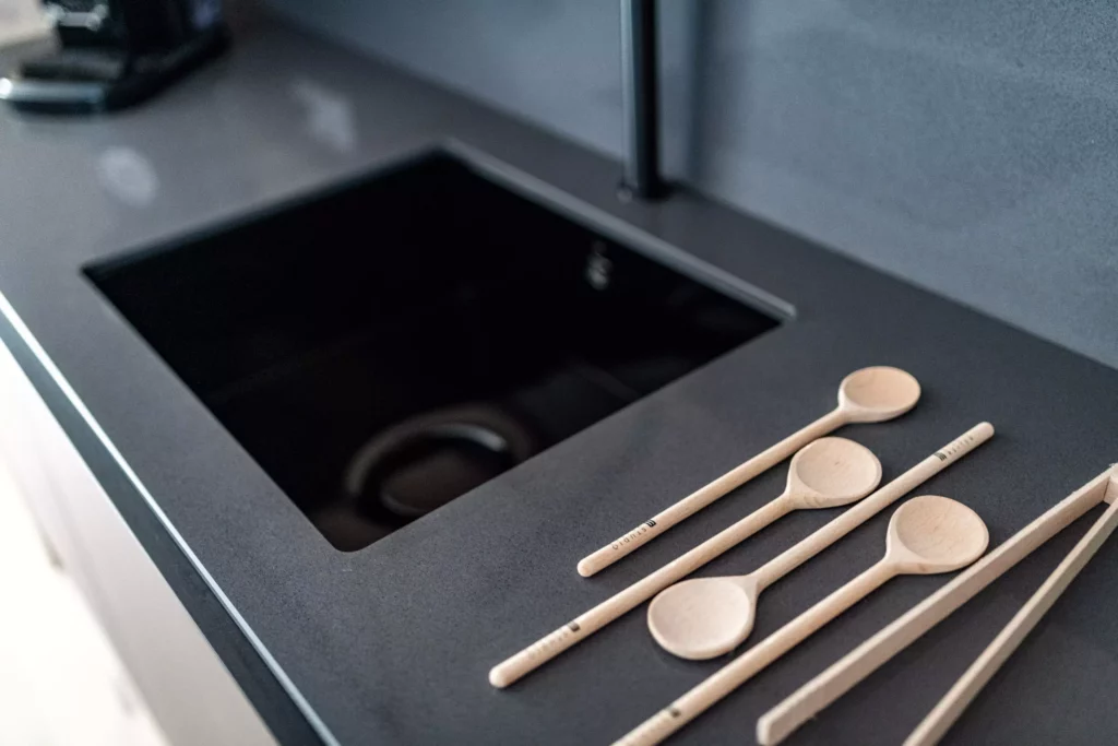 Schwarze Küchenarbeitsplatte mit integriertem Kochfeld und vier Holzlöffeln, modernes Design, M-Studio Reiter, Möbelstudio