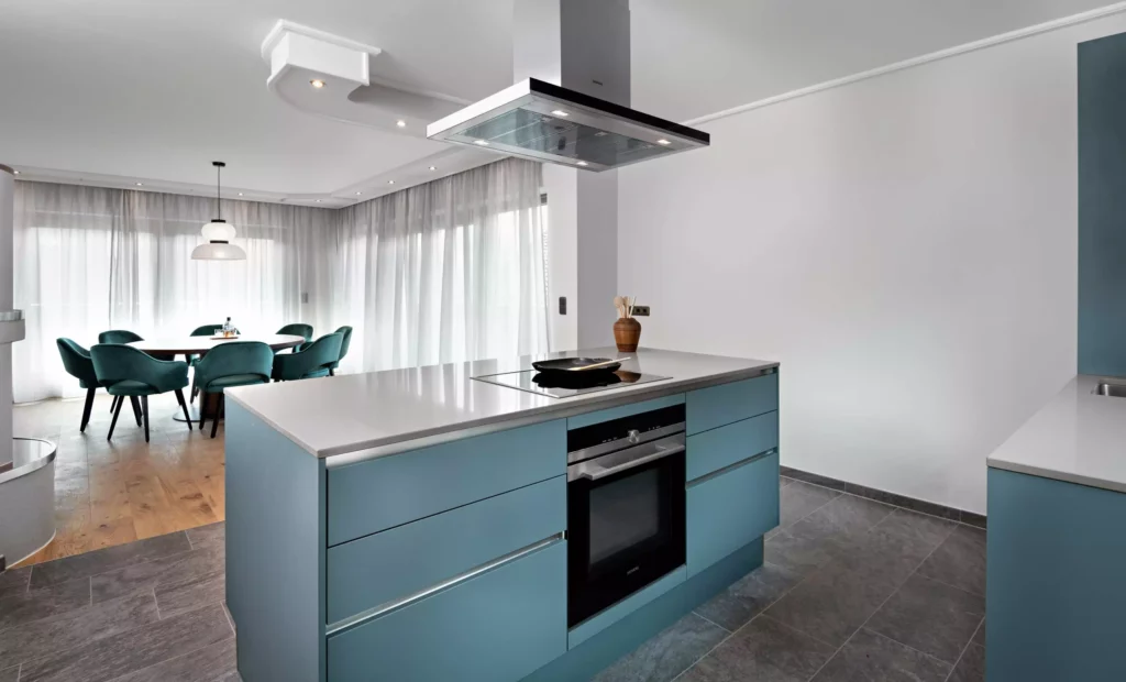 Moderne Küche mit blauen Kücheninseln, Kochfeld, Dunstabzug und Essbereich mit grünem Polsterstuhl-Set vor, Riva1920