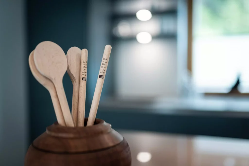 Holzlöffel mit Studio Reiter Schriftzug in einem Holzgefäß vor unscharfem Küchenhintergrund als Detail der, Riva1920