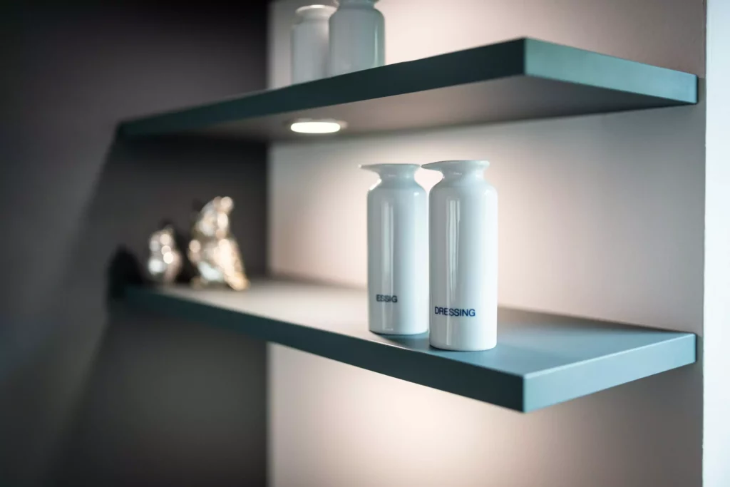 Zwei weiße Keramikflaschen mit Beschriftung Essig und Dressing auf grauem Wandregal mit indirekter Beleuchtung in, Riva1920