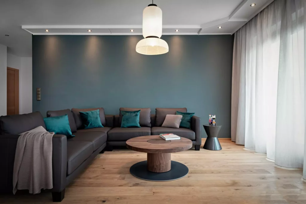 Modernes Wohnzimmer mit dunkelgrauem Ledersofa, runden Holztisch von Riva1920, blauen Kissen und grauer Wand im