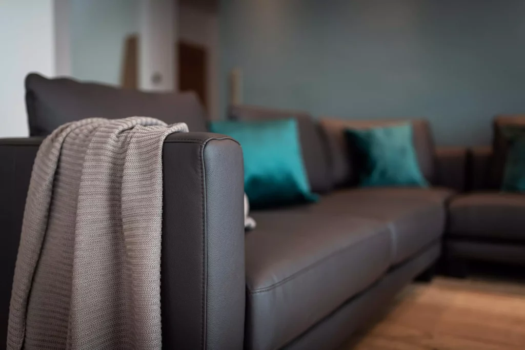 Nahaufnahme eines dunkelbraunen Ledersofas mit grauer Strickdecke am Armlehne und türkisfarbenen Kissen im modernen, Riva1920