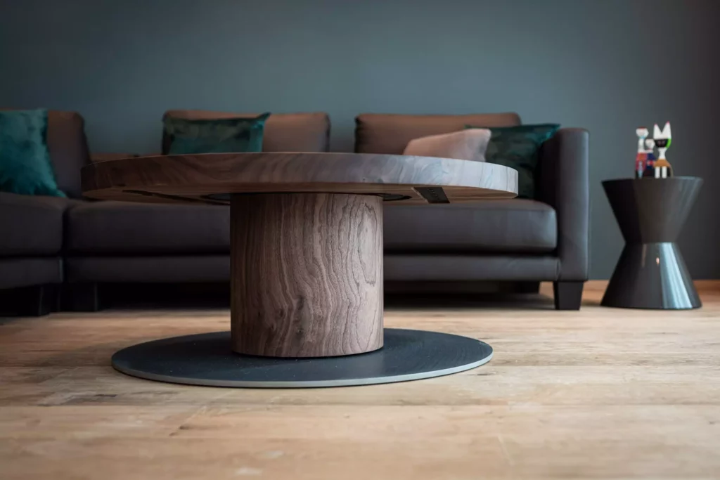 Runder Couchtisch aus Holz mit schwarzer Bodenplatte vor grauem Ledersofa und modernem Beistelltisch mit, Riva1920