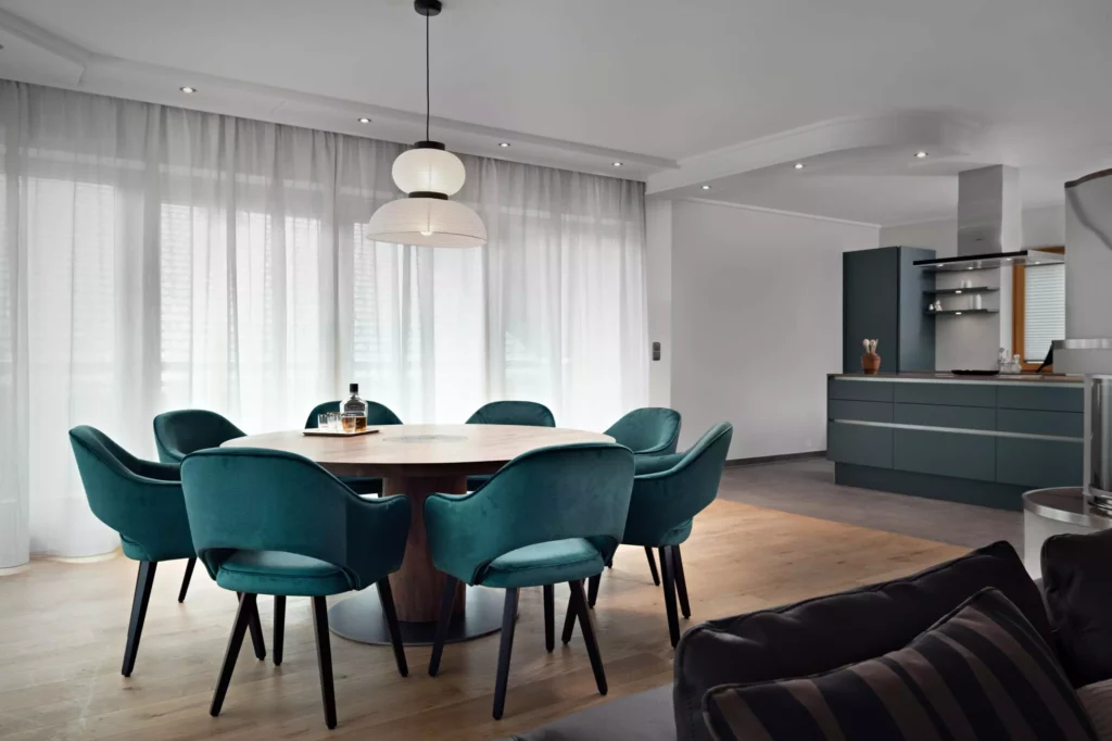 Moderner Essbereich mit runden Riva1920 Holztisch und sechs grünen Samtstühlen in offenem Wohnraum mit Küche und heller