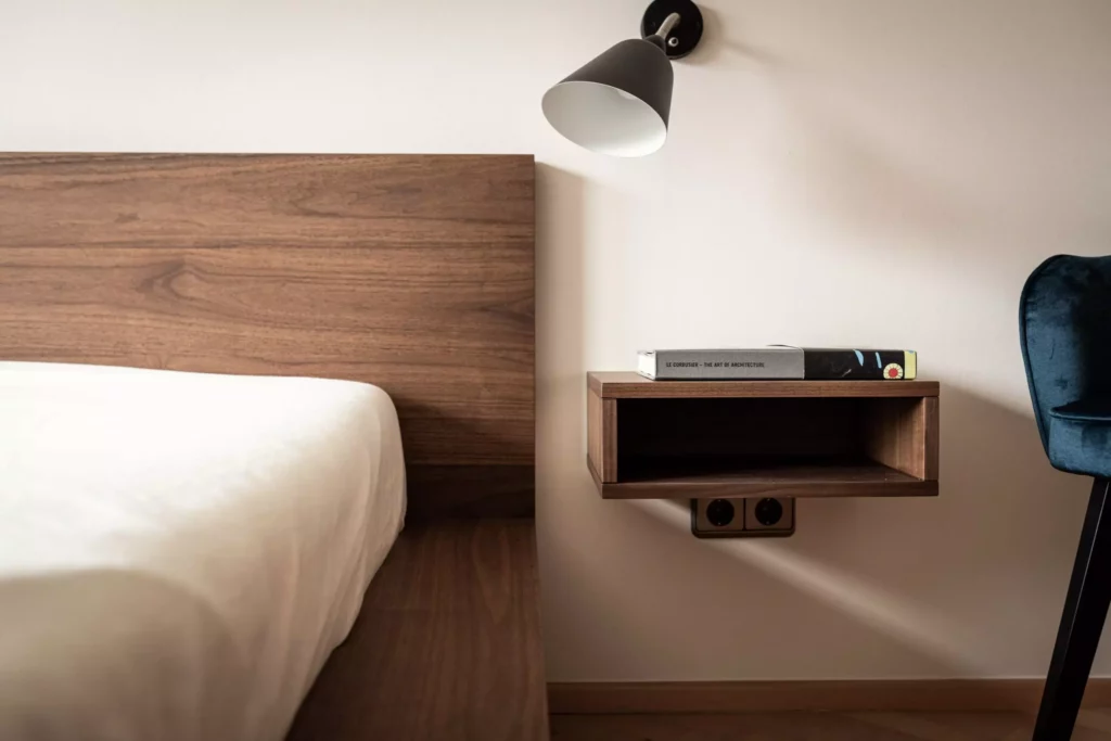 Schlafzimmer mit maßgefertigtem Riva1920 Holzbett und schwebendem Nachttisch, Wandlampe und Designstuhl in Salzburg