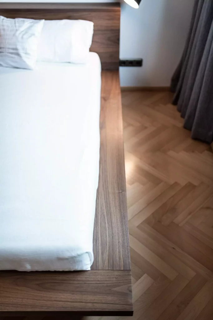 Bett mit weißer Bettwäsche und maßgefertigtem Holzrahmen aus Nussbaumholz auf Fischgrätparkett in modernem, Riva1920