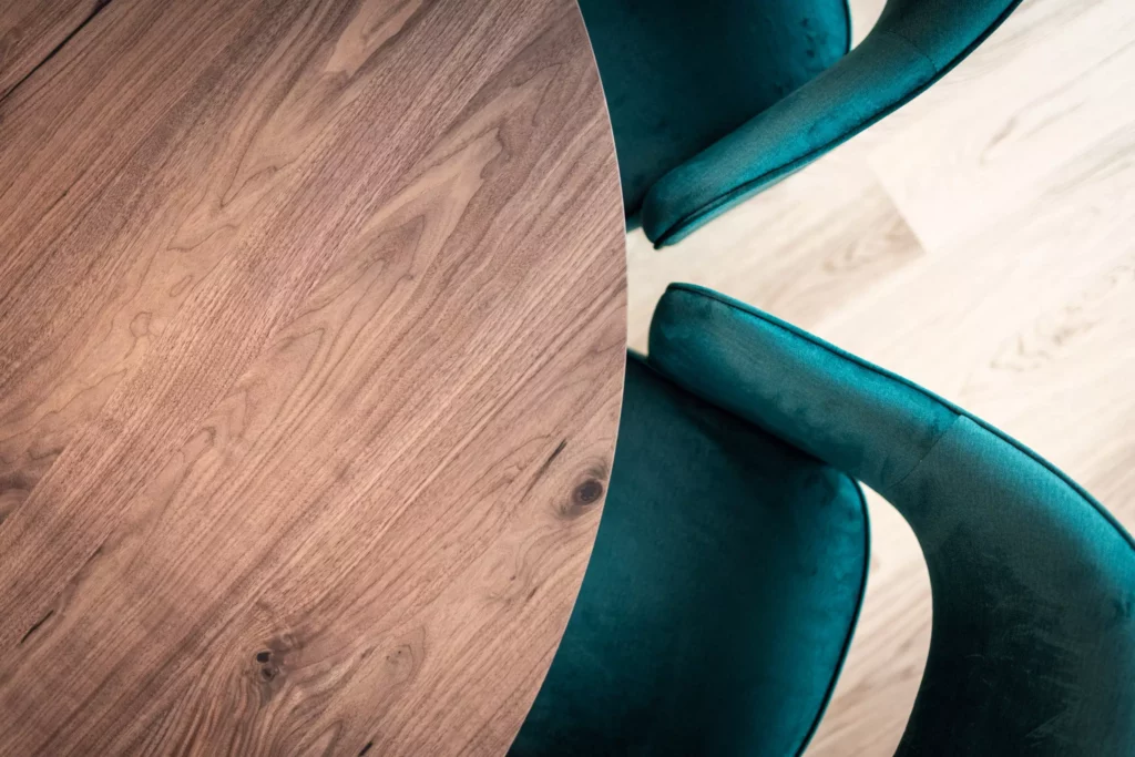 runder Holztisch mit sichtbarer Maserung und zwei dunkelgrünen Samtstühlen auf hellem Holzboden in modernem, Riva1920
