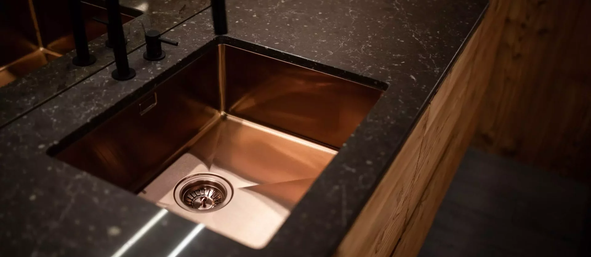 Moderne Küchenarbeitsplatte mit eingelassener kupferfarbener Spüle, schwarzem Wasserhahn und Holzfronten, Minotti