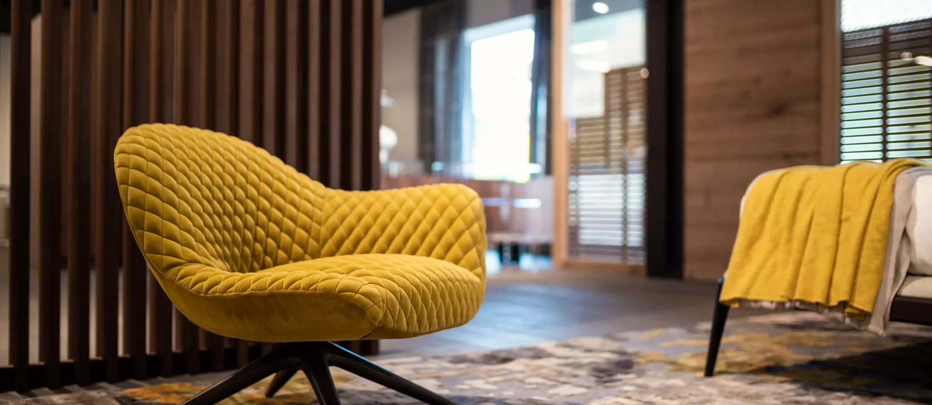 Gelber Poliform Sessel mit Steppung auf Teppich vor Holzlamellenwand in modernem Möbelstudio mit Wohnraumplanung und, Minotti