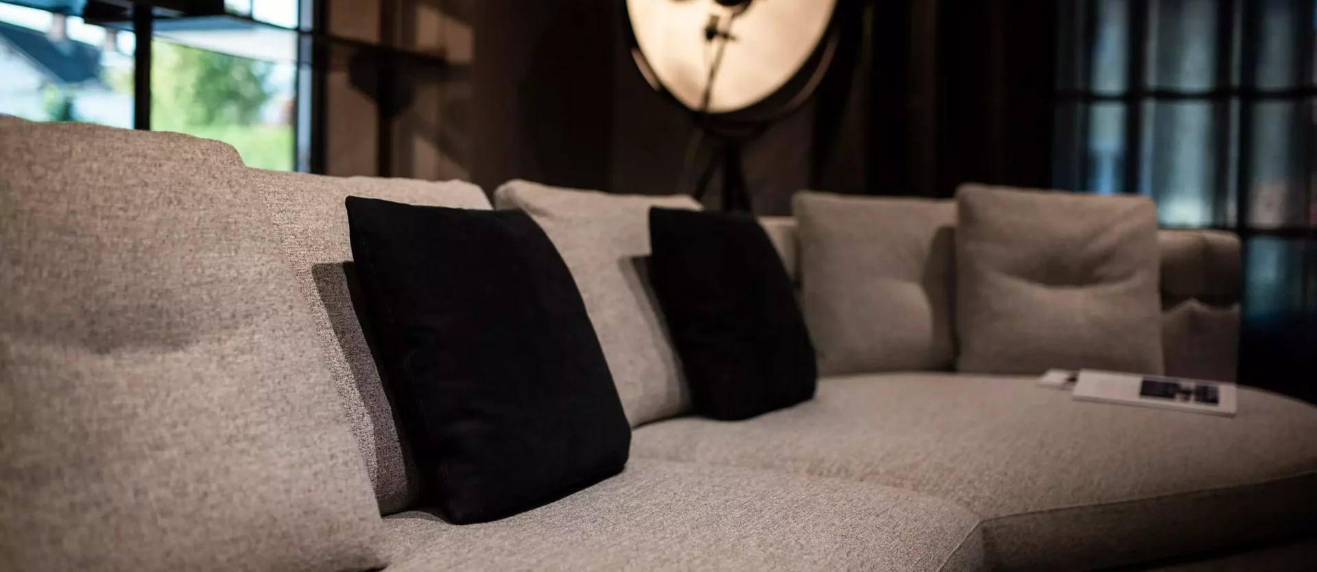 Modernes Wohnzimmer mit grauem Minotti Sofa, schwarzen Kissen, Stehlampe und dunklen Vorhängen im Möbelstudio Showroom