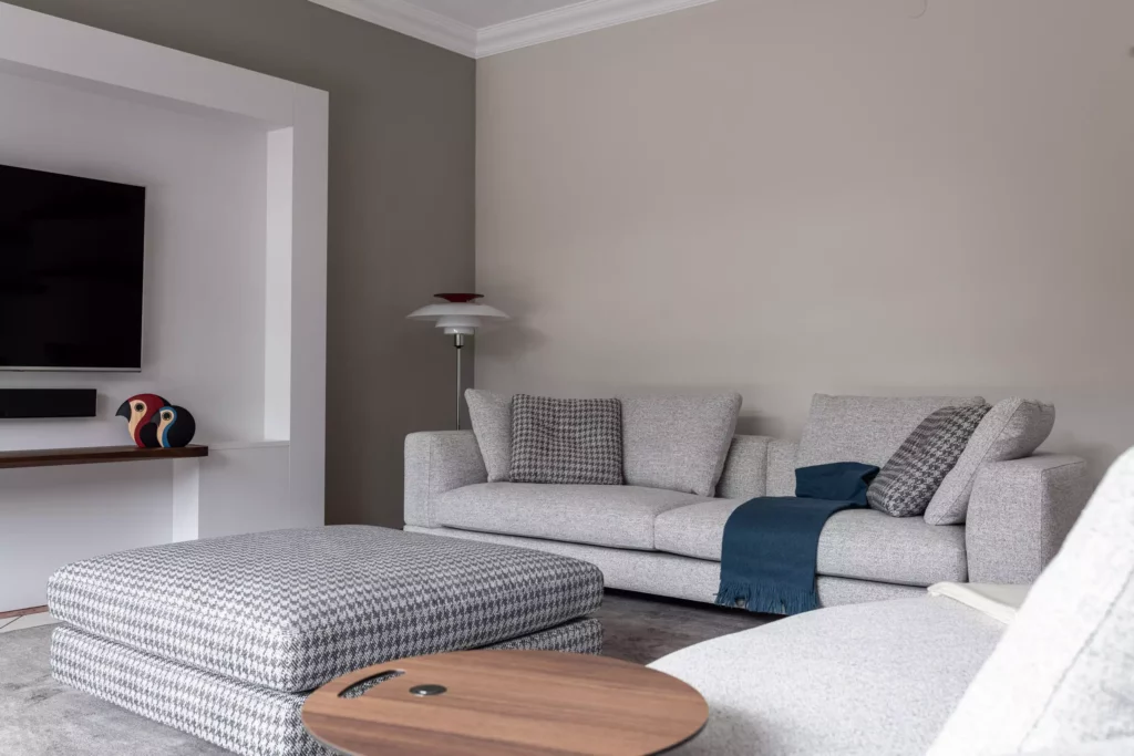 Modernes Wohnzimmer mit grauem Minotti-Sofa, Hahnentritt-Ottomane, blauem Plaid, Holzbeistelltisch und TV-Wand im